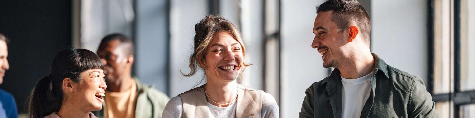 A group of young adults, possibly students or professionals, are conversing and collaborating in a bright, modern co-working environment.